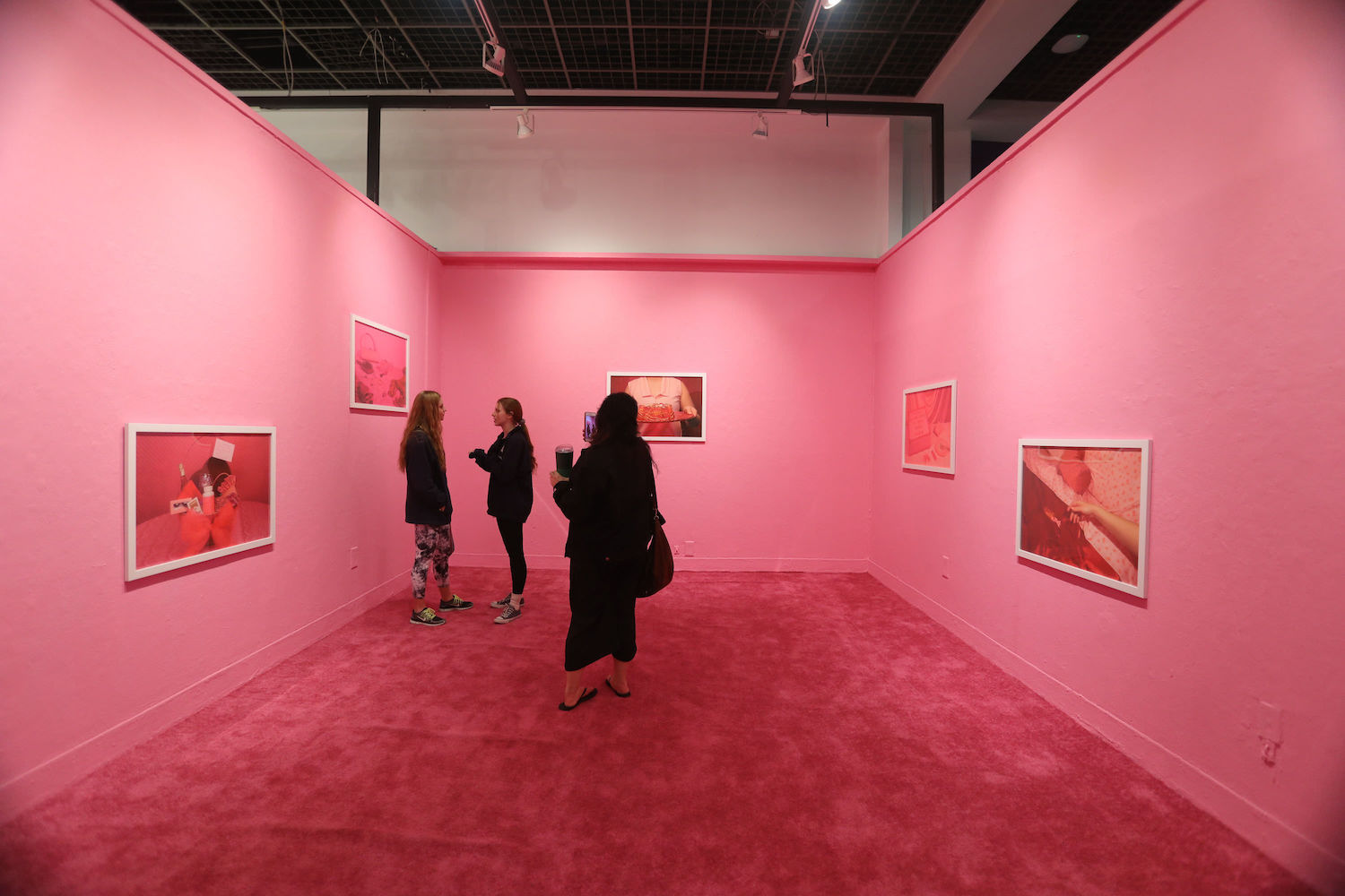 A gallery painted pink with red carpet and images on the walls. 