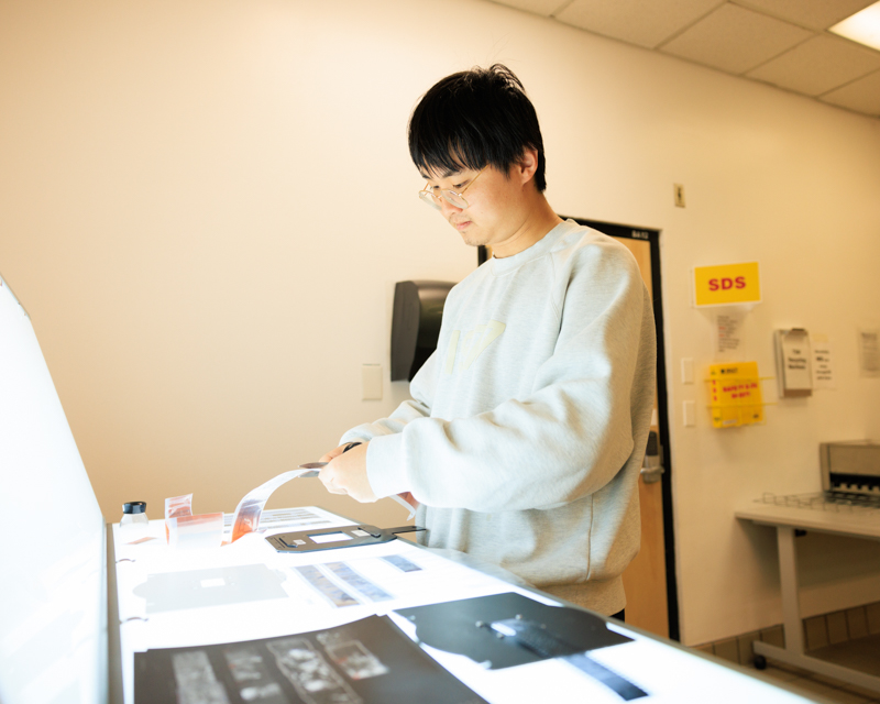 Student cutting photo negatives on light table in photo lab. 