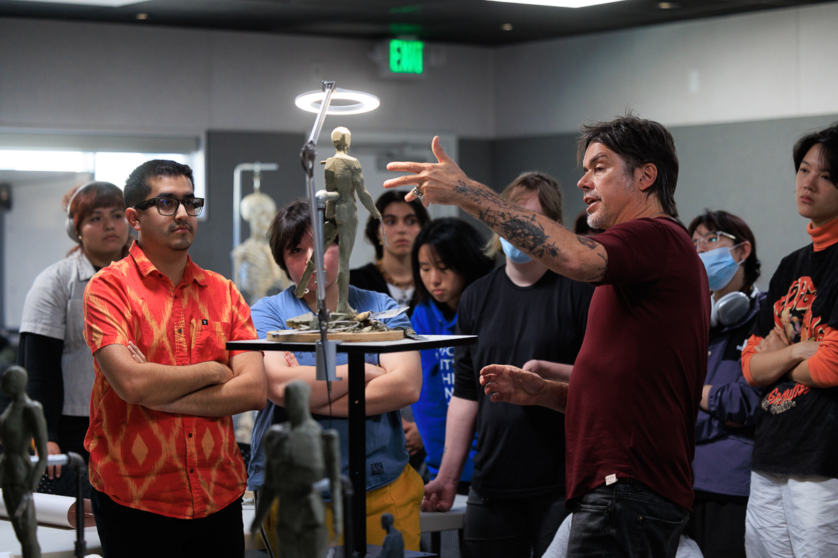 Teacher pointing at a clay figure sculpture example to a group of students. 