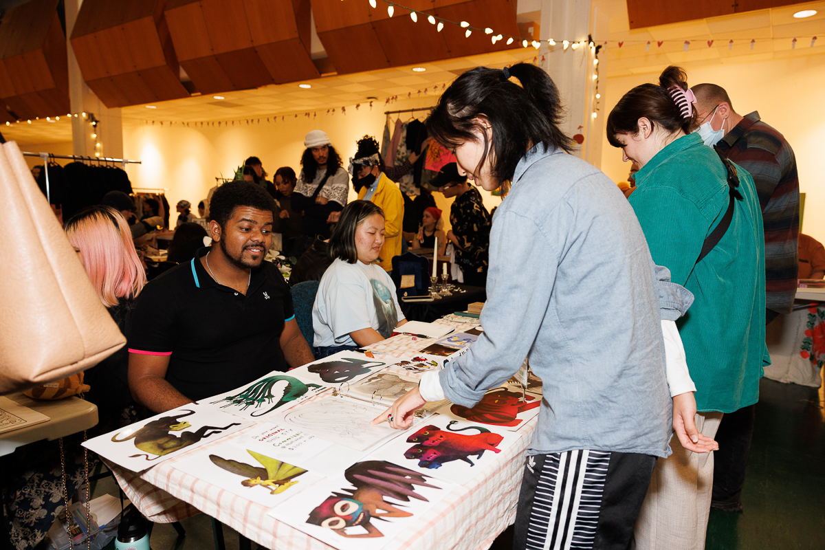  People look at animation drawings displayed on a table in a crowded room during a portfolio fair 