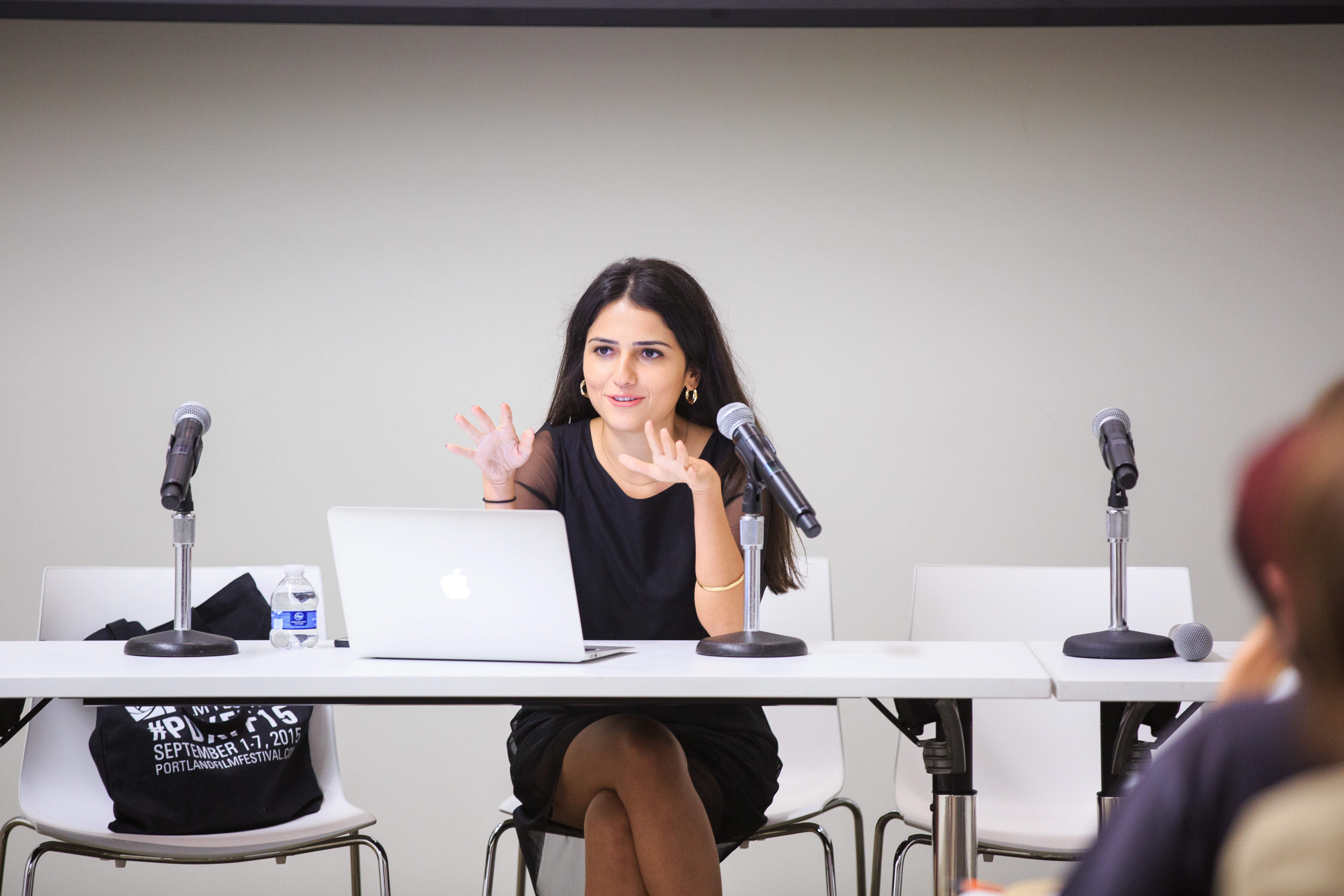 Woman with dark hair and black dress sitting at a table speaking into a microphone