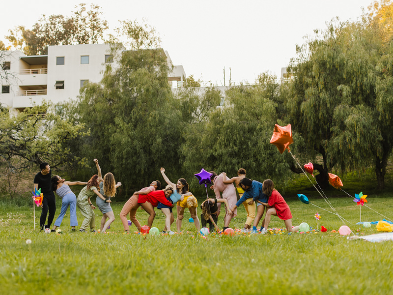 group of people dancing in the middle of a field; dancers are wearing different colors 