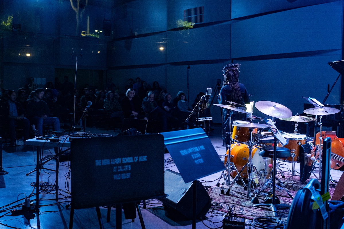 Indoor music performance with an audience and a drummer on stage.