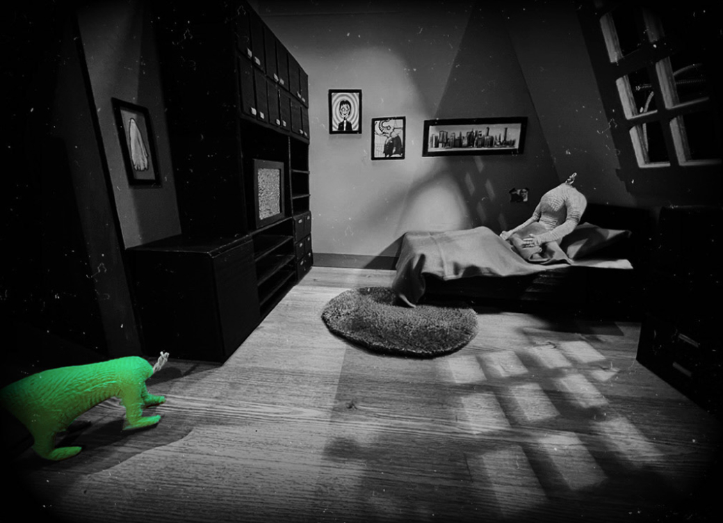 A shadowy room, in black and white, with a bright green four-legged, headless, dog-size creature in the lower left corner. A headless figure, stuffed like a doll, sits in a bed in the opposite corner.