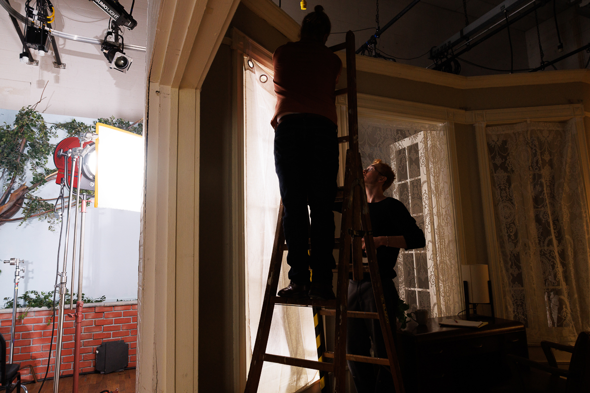 Two people working on a studio set adjusting the drapery