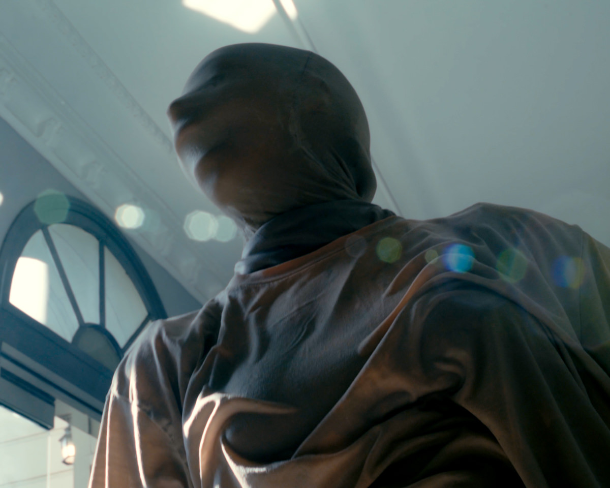 Slightly out-of-focus image of a person’s head, seen from below, shrouded in translucent fabric.