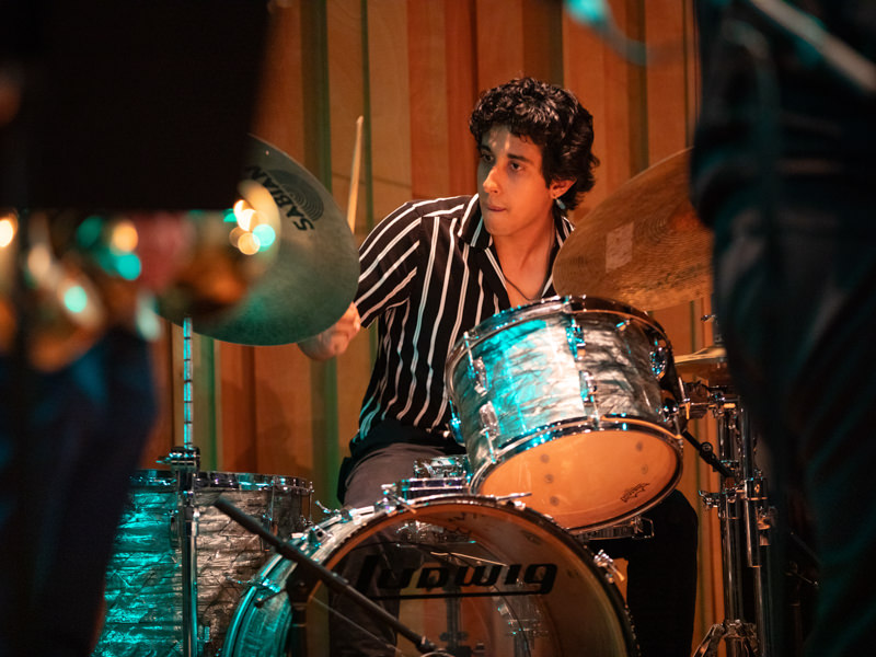 A man wearing a black-and-white striped shirt plays a drum set.