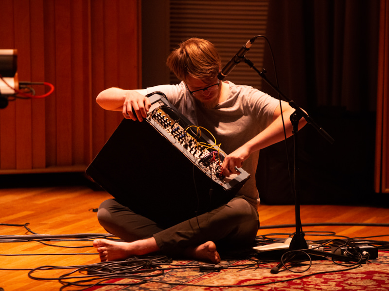 A person sits cross legged with an amp in their lap. They manipulate it with their hands. 