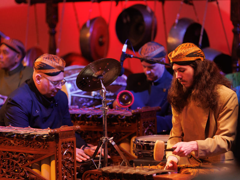 Several musicians in hats sit to perform Gamelan