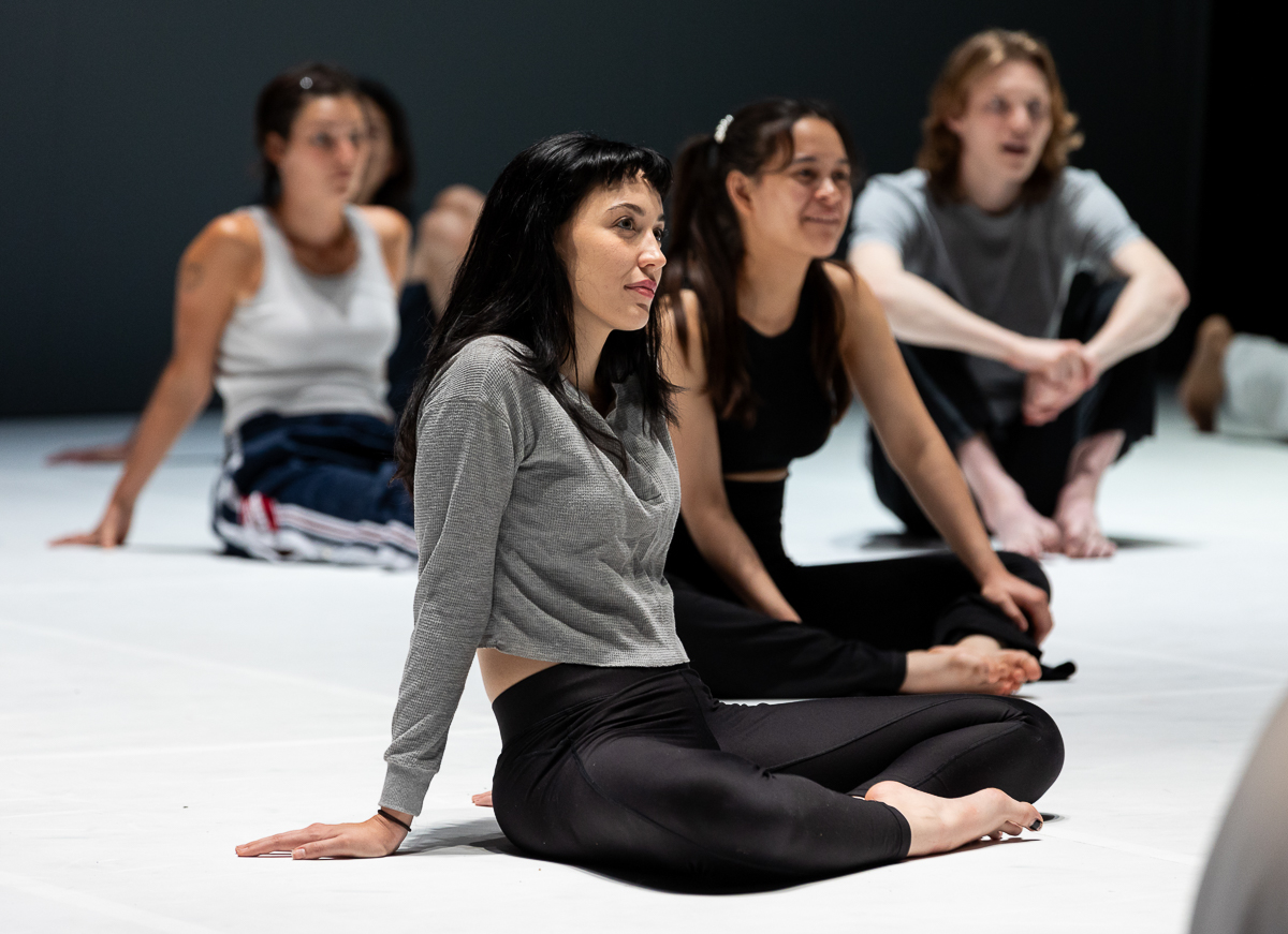 Small group of students in an acting class sitting cross-legged on a stage floor