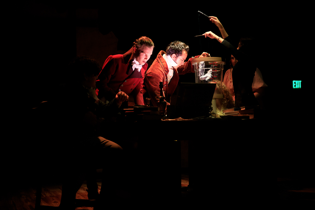 People on a dark stage observing a device