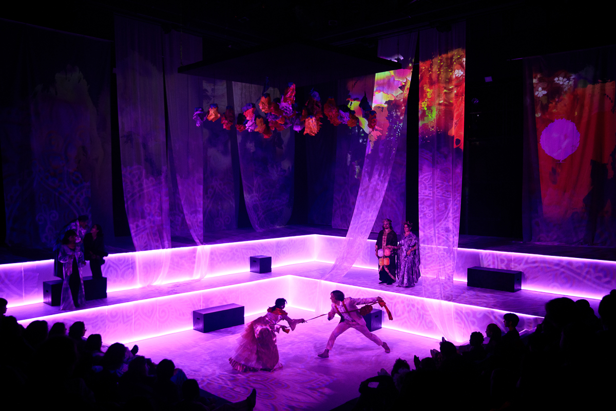 A large stage with purple lighting as two people center stage interact