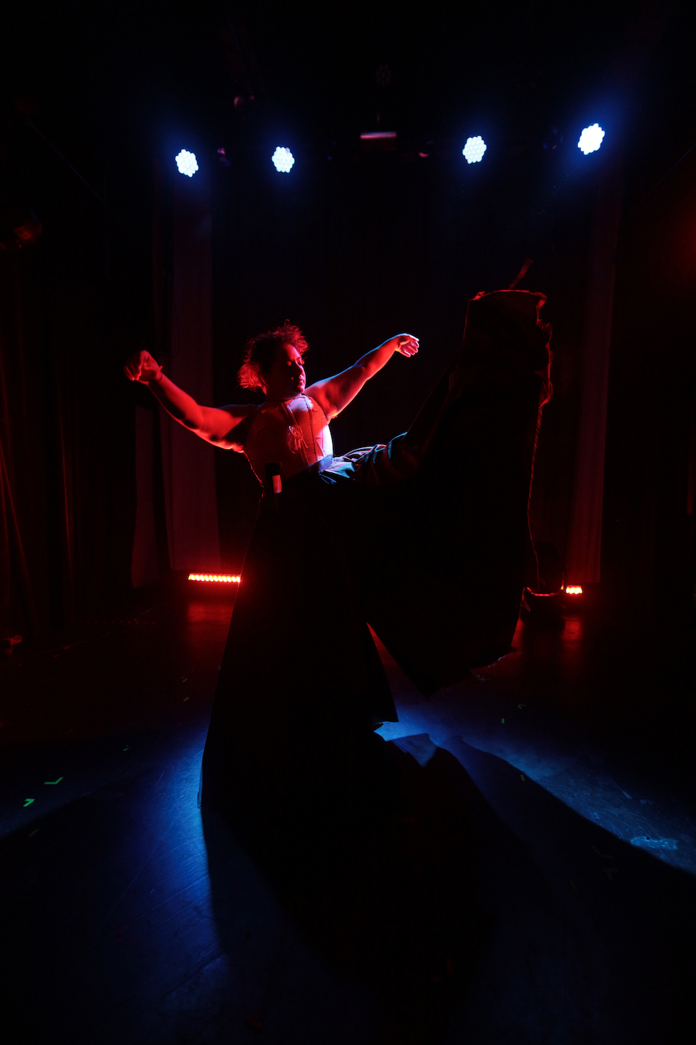 A person dances in a long skirt, in a room with dramatic lighting