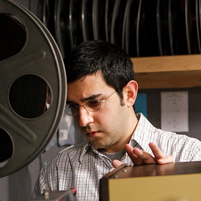 Man examines equipment in a film projection room beside a large film reel.