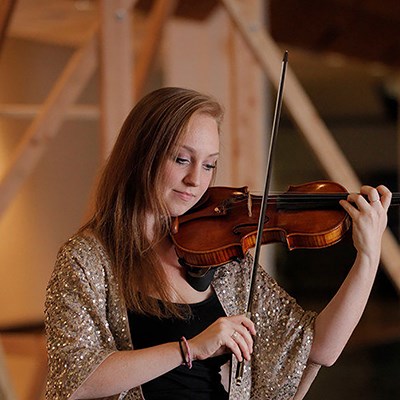 Person playing the violin indoors, wearing a sparkly shawl.