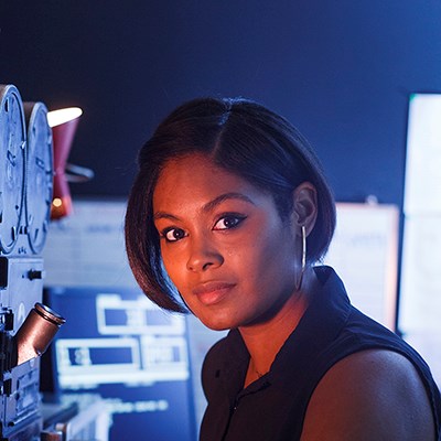 Woman in a dimly lit technical room with equipment and screens.