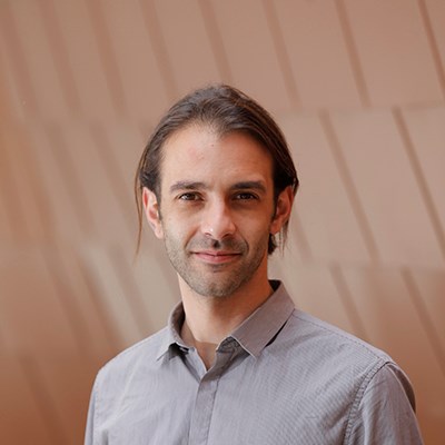 Person with long dark hair wearing a gray shirt against a light brown panel background.