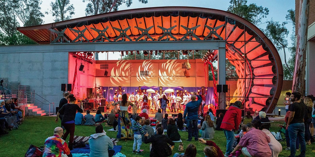 Outdoor performance at an amphitheater with a colorful stage and seated audience.