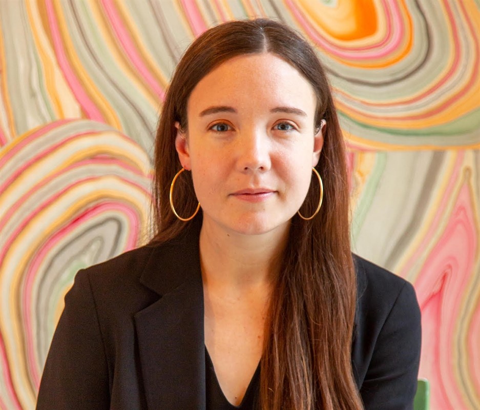 Person with long brown hair and hoop earrings against a colorful abstract background with swirling patterns.