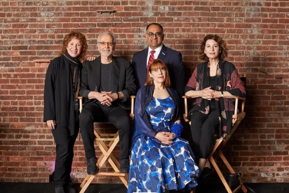 Photograph of 5 people with a brick wall in the background