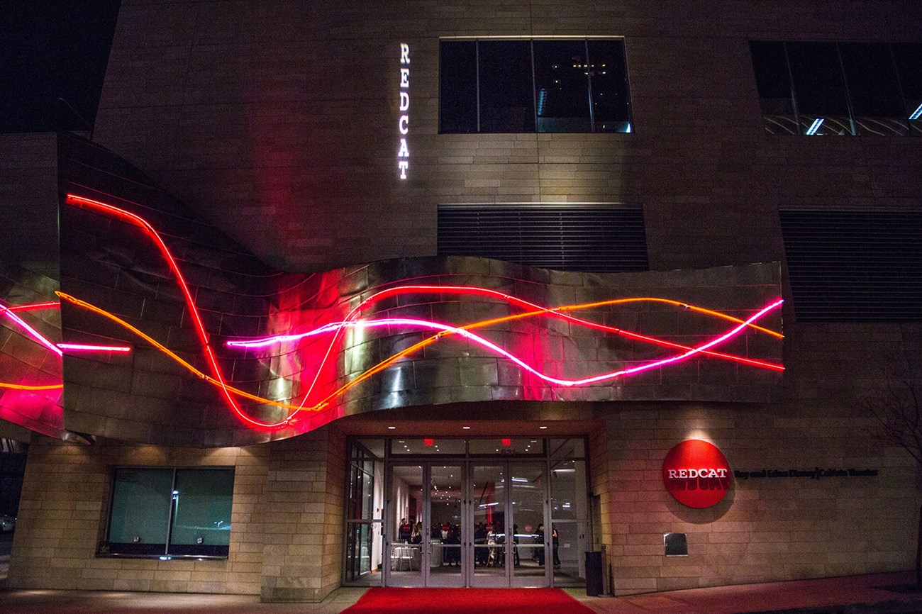 The REDCAT building exterior at night with neon lights and red carpet entrance.