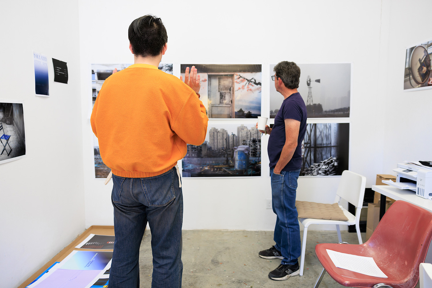 Two people stand in a room discussing photographs on a wall.