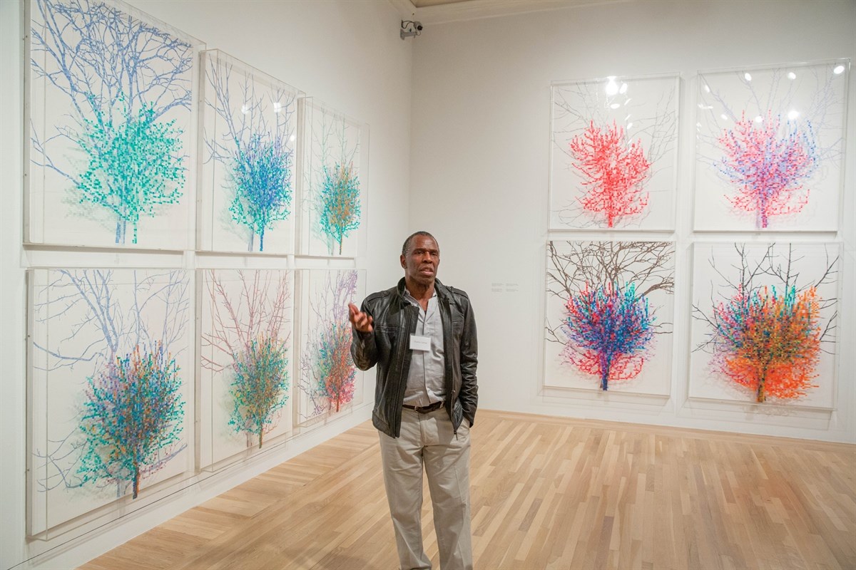 Art gallery with colorful tree-themed artworks and a person standing in front.