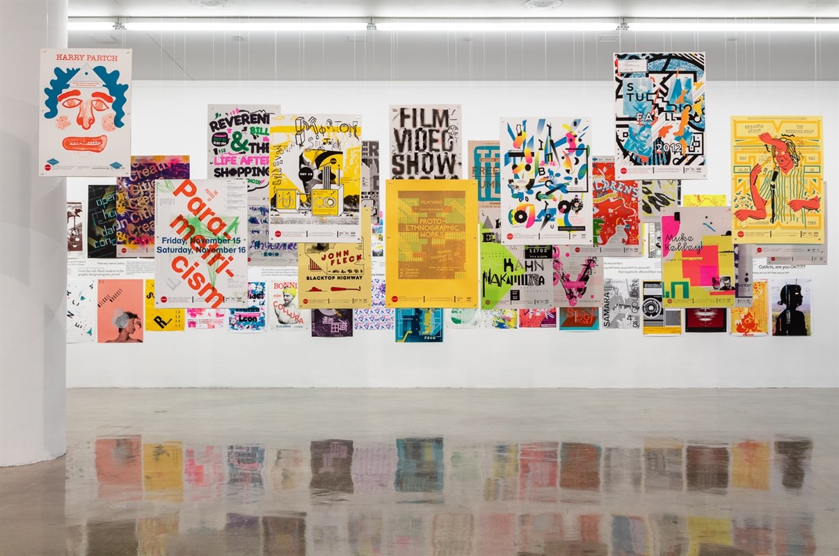 An art installation featuring a collection of colorful posters displayed on a white wall, each showcasing different designs and colors.