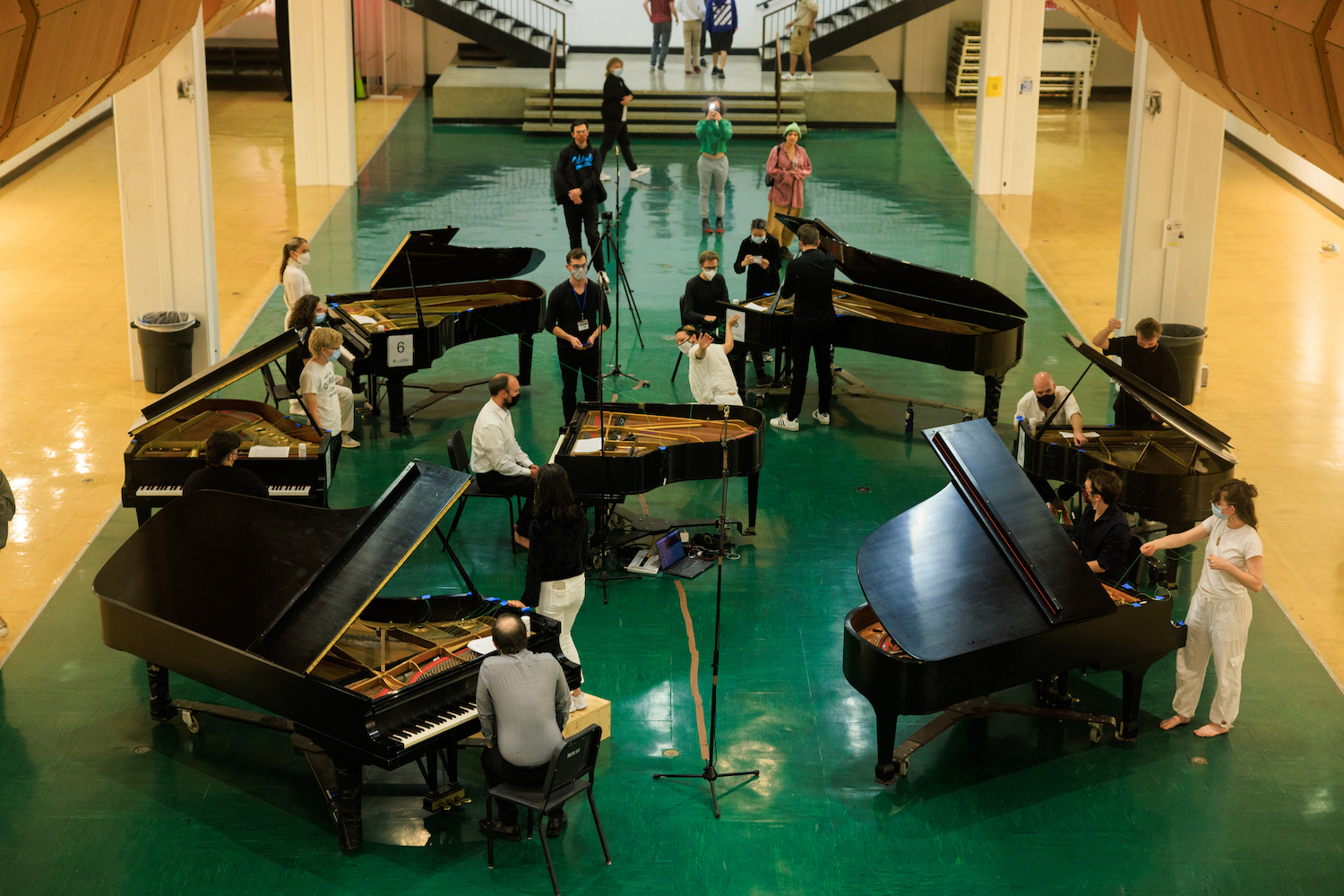 Seven pianos in a circle, each with players and dancers moving between them. 