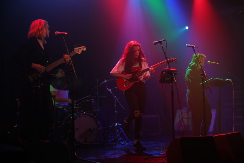 A band performing on a stage with colorful red, blue, and green lighting effects.