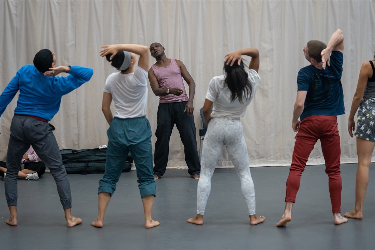 A group of dancers practicing movements in front of a light curtain, with an instructor leading