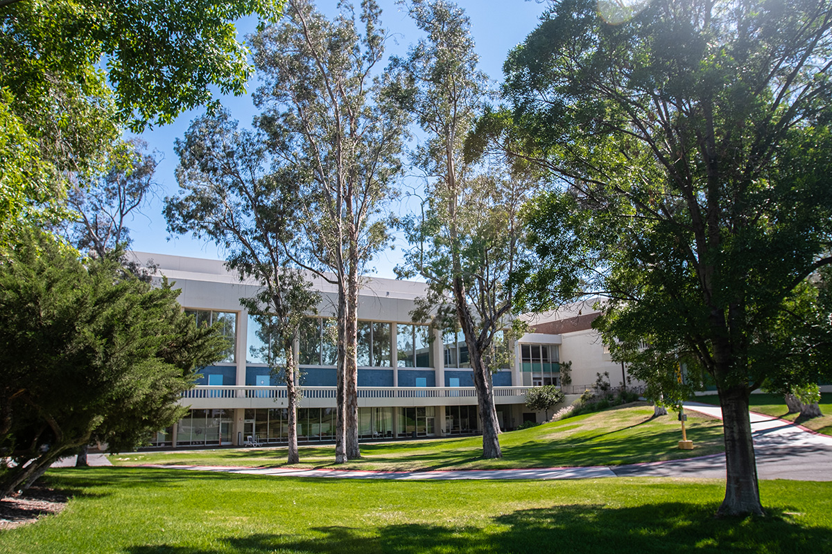 A white modern building with large windows surrounded by trees and a green lawn on a sunny day.