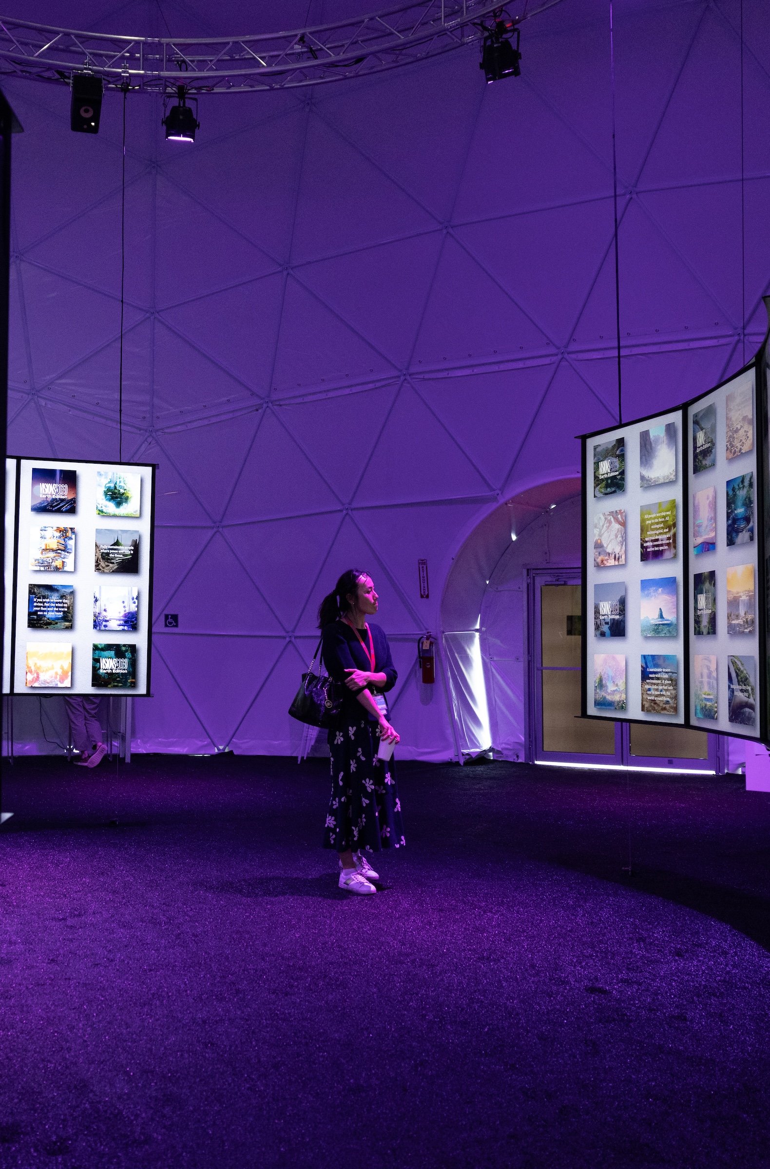 A person stands inside a purple-lit dome, viewing a screen with a grid of images.