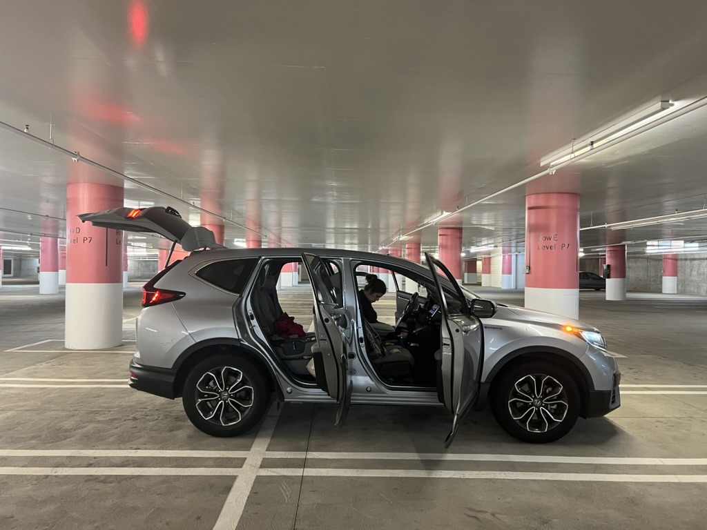 Silver SUV with open doors in an indoor parking garage, alongside red and white columns.