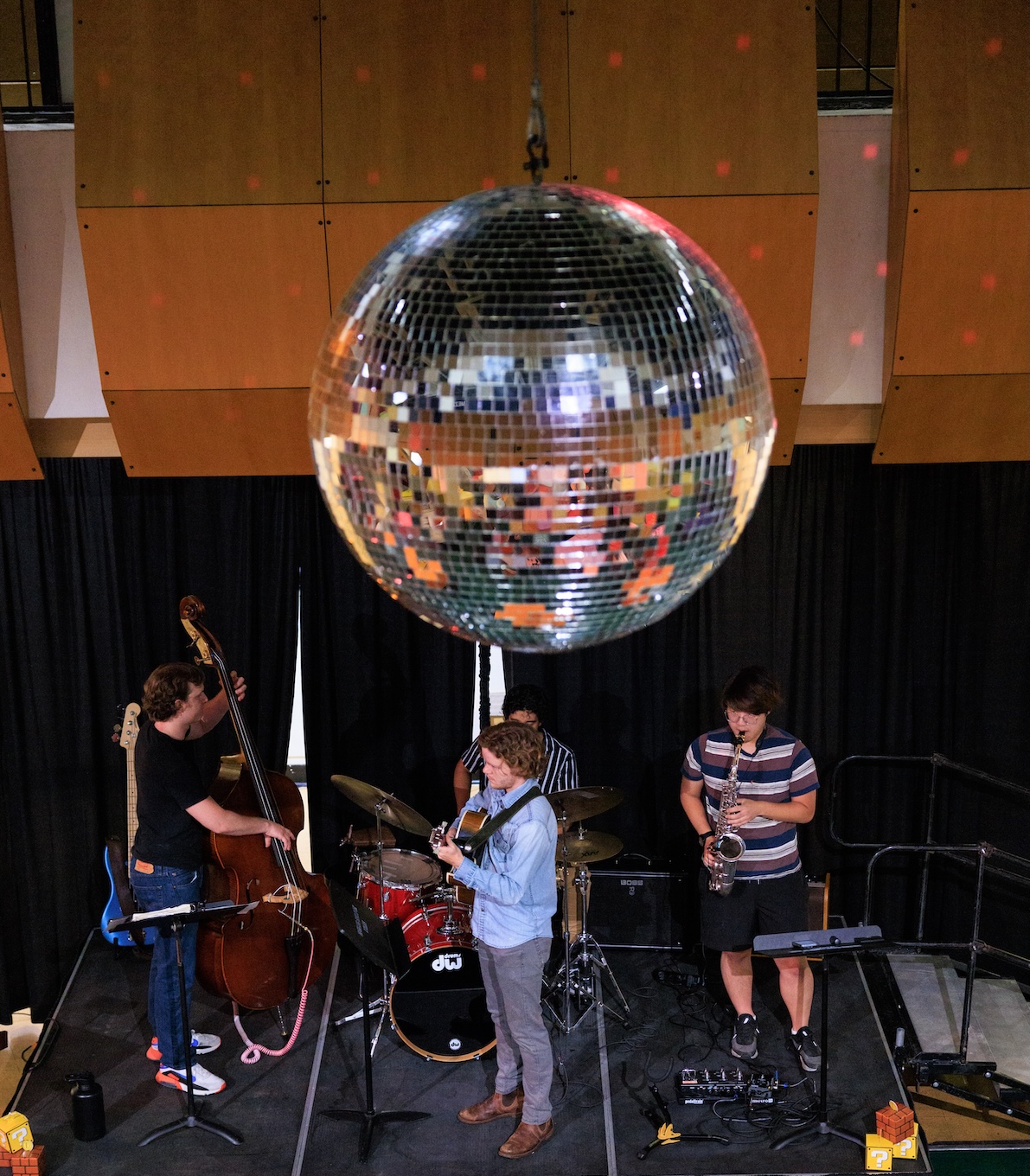A musical ensemble performs on stage beneath a large disco ball.
