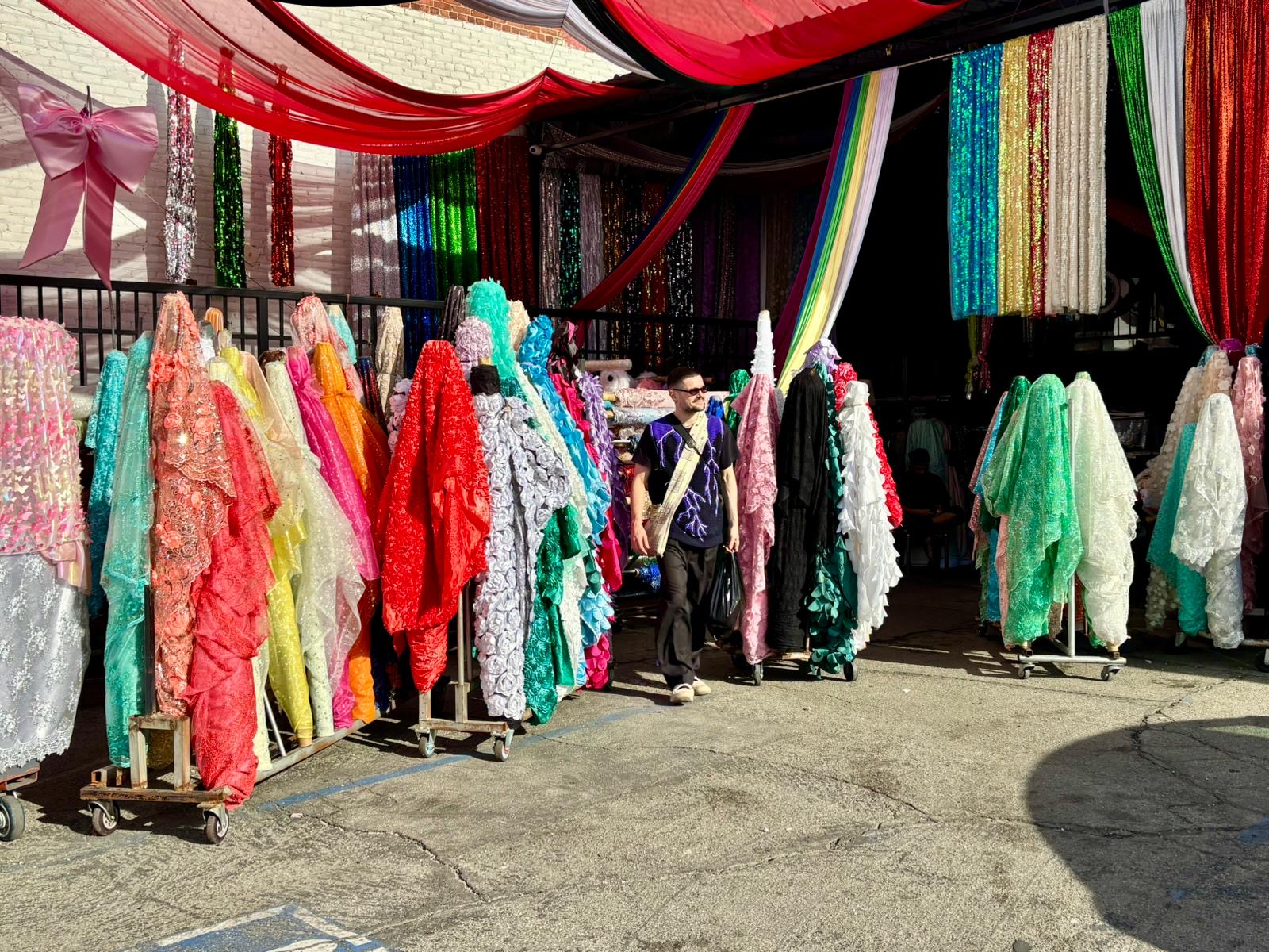 Colorful fabric displays in an outdoor market, with a person walking past.