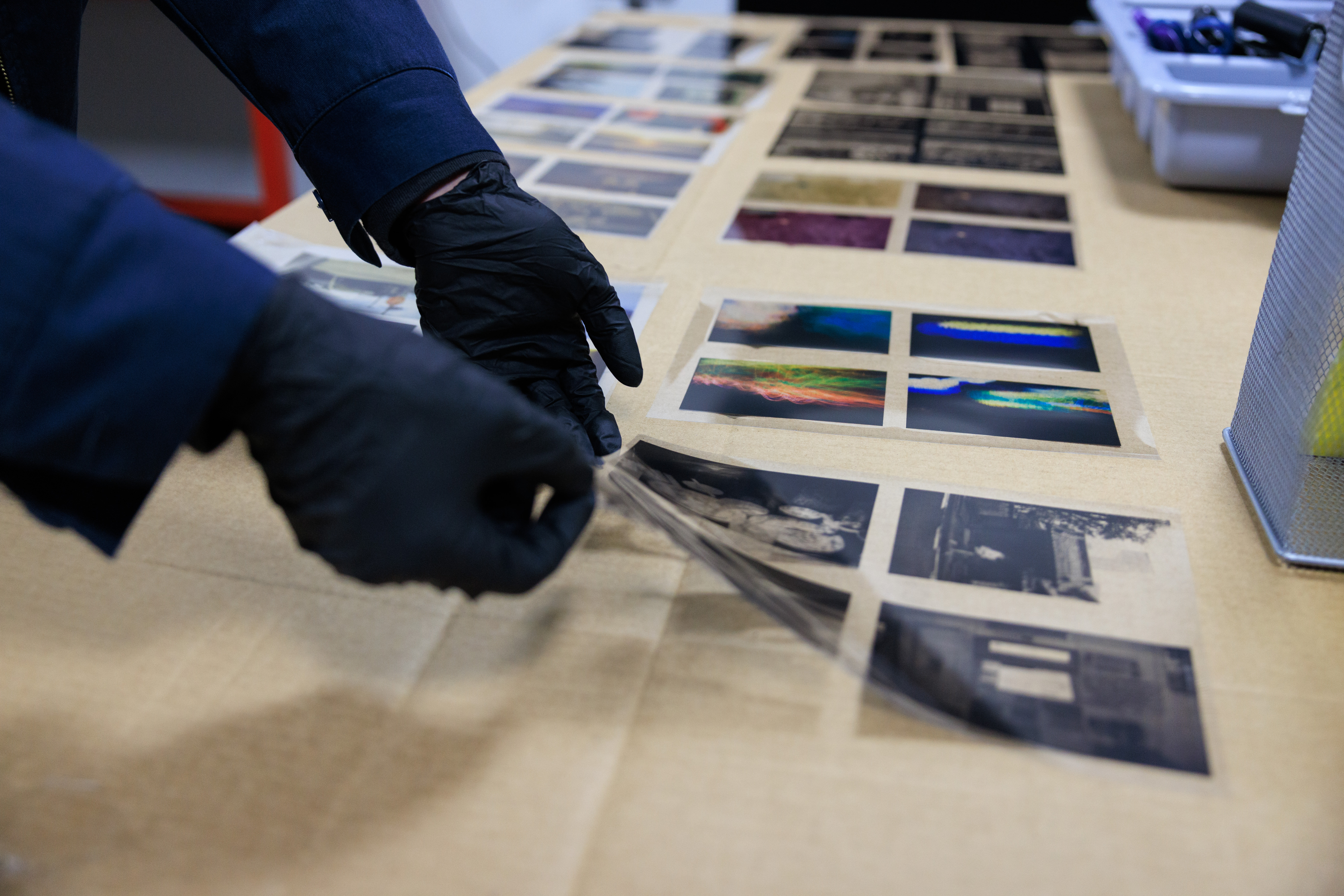 Gloved hands arrange colorful and monochrome photographic prints across a worktable.