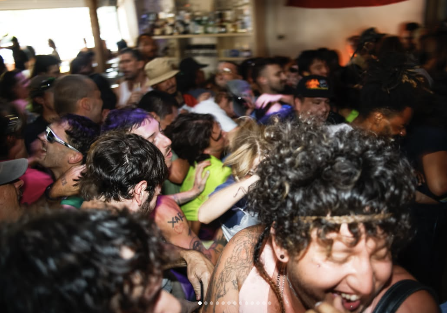 A tightly packed, lively indoor crowd with people dancing or moving through a dimly lit room.