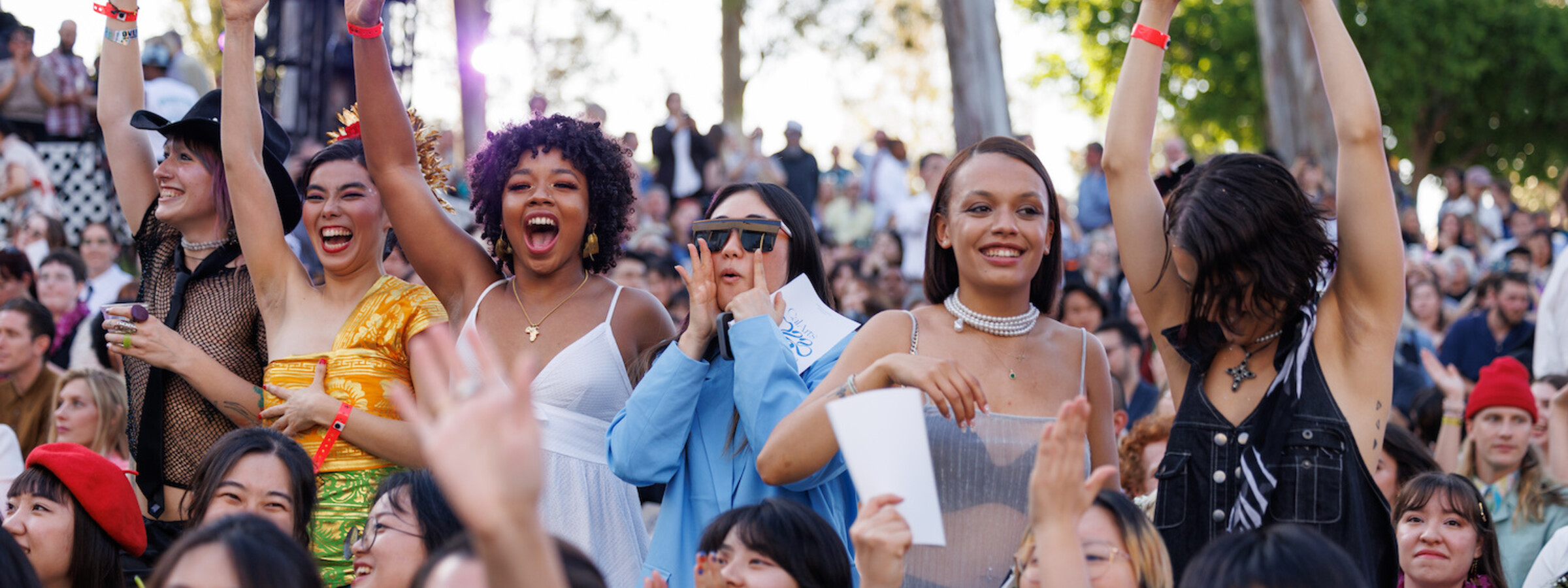 Students in festive clothes stand up and cheer at CalArts graduation