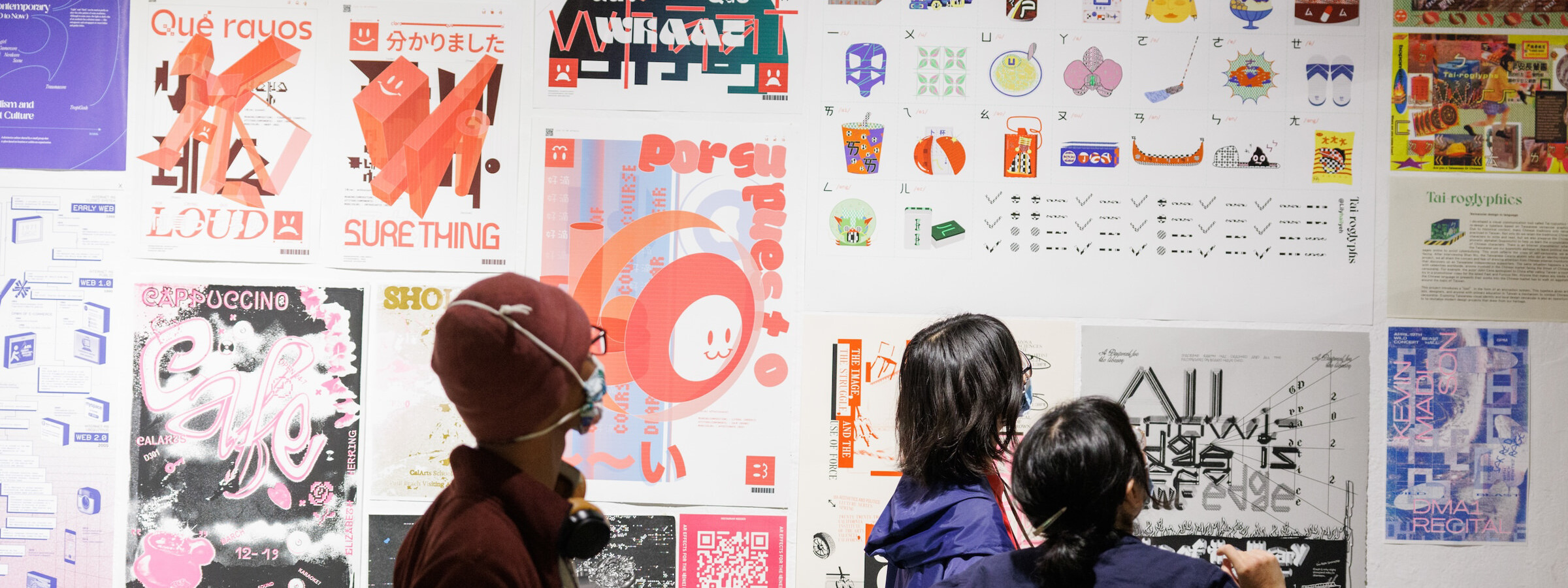 Three people standing in a gallery observing a wall filled with art posters