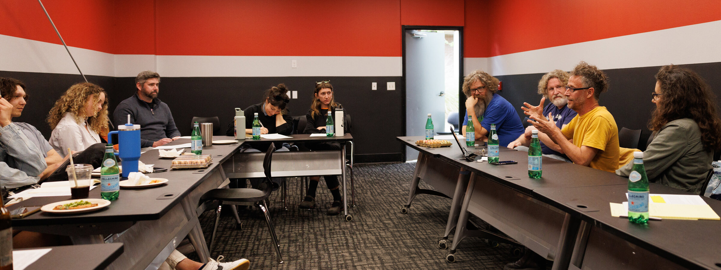 Group of students and faculty in intense discussion in a room with bright red walls