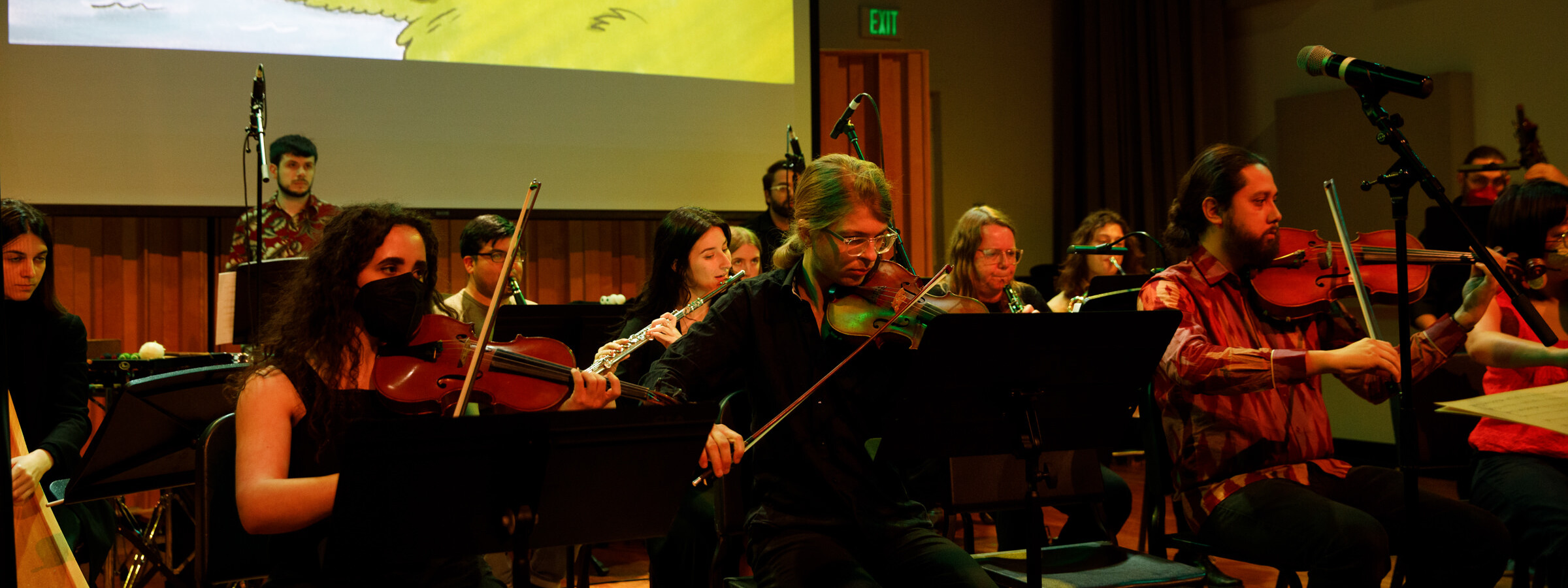 A group of musicians playing instruments on a small stage, while an animation is playing on a screen behind them. 