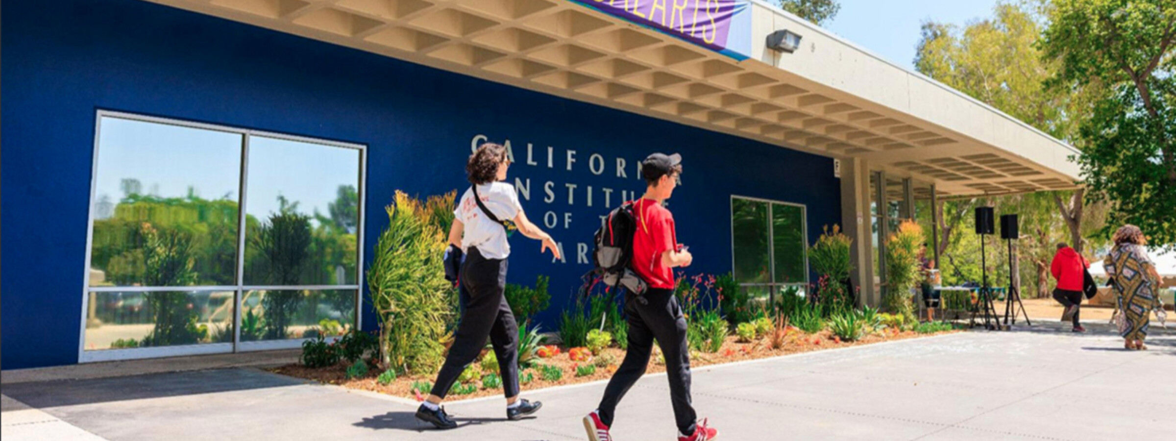 Two students walking in front of building with Welcome to CalArts banner