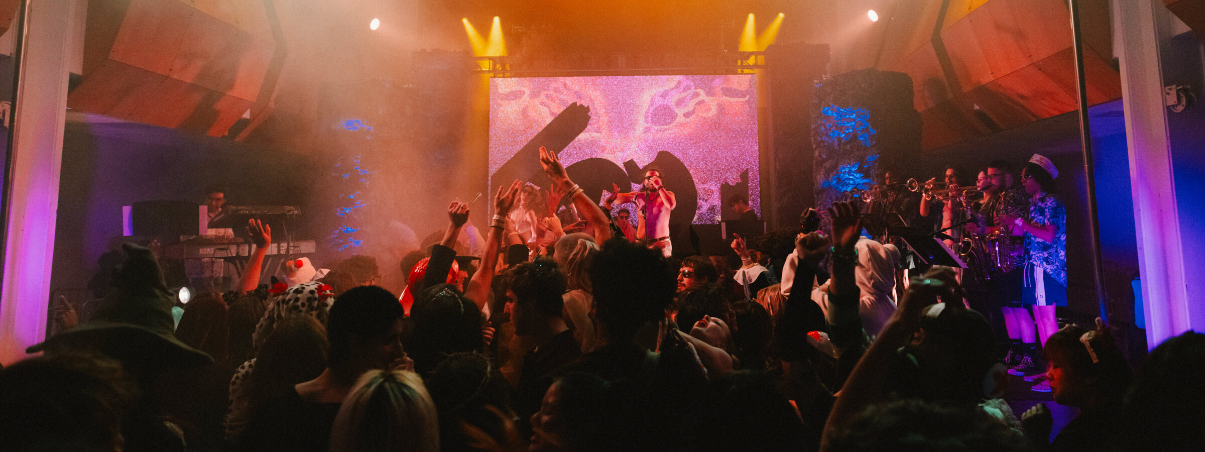 A brightly lit stage in a dark room with a band performing with an audience dancing in the foreground