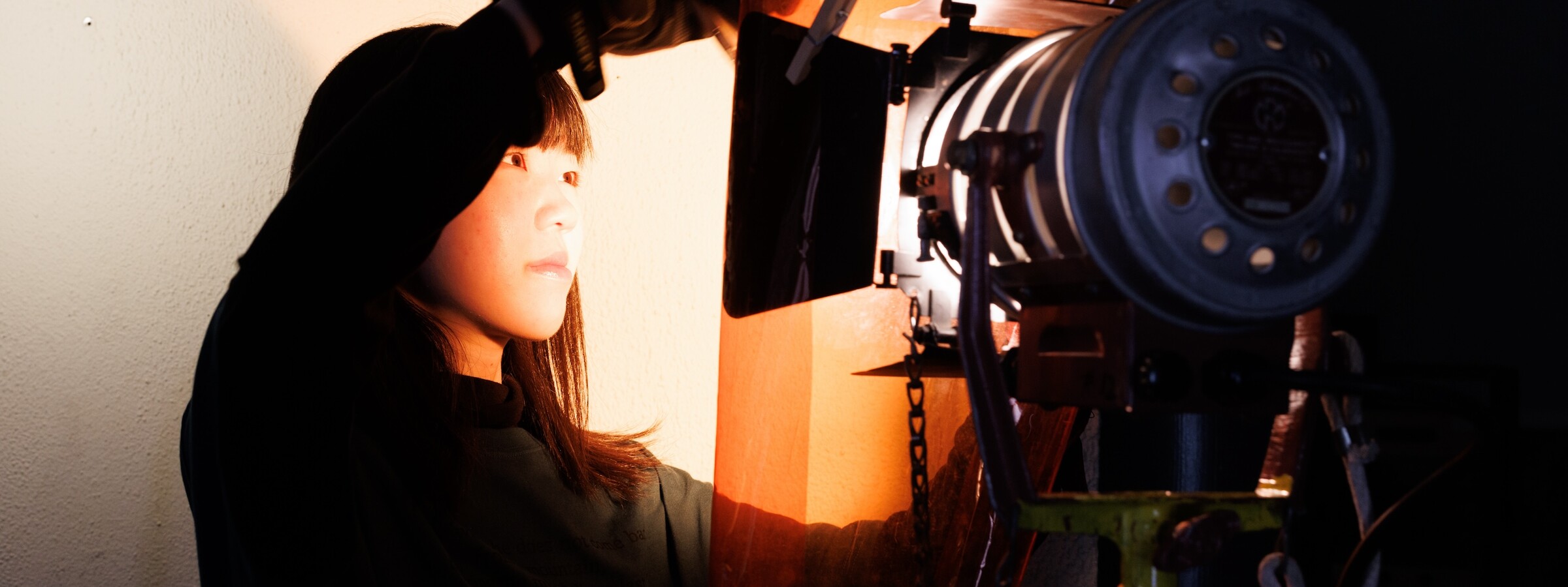 A college student adjusts a cinematic light, which shines on her face and creates an orange glow around her