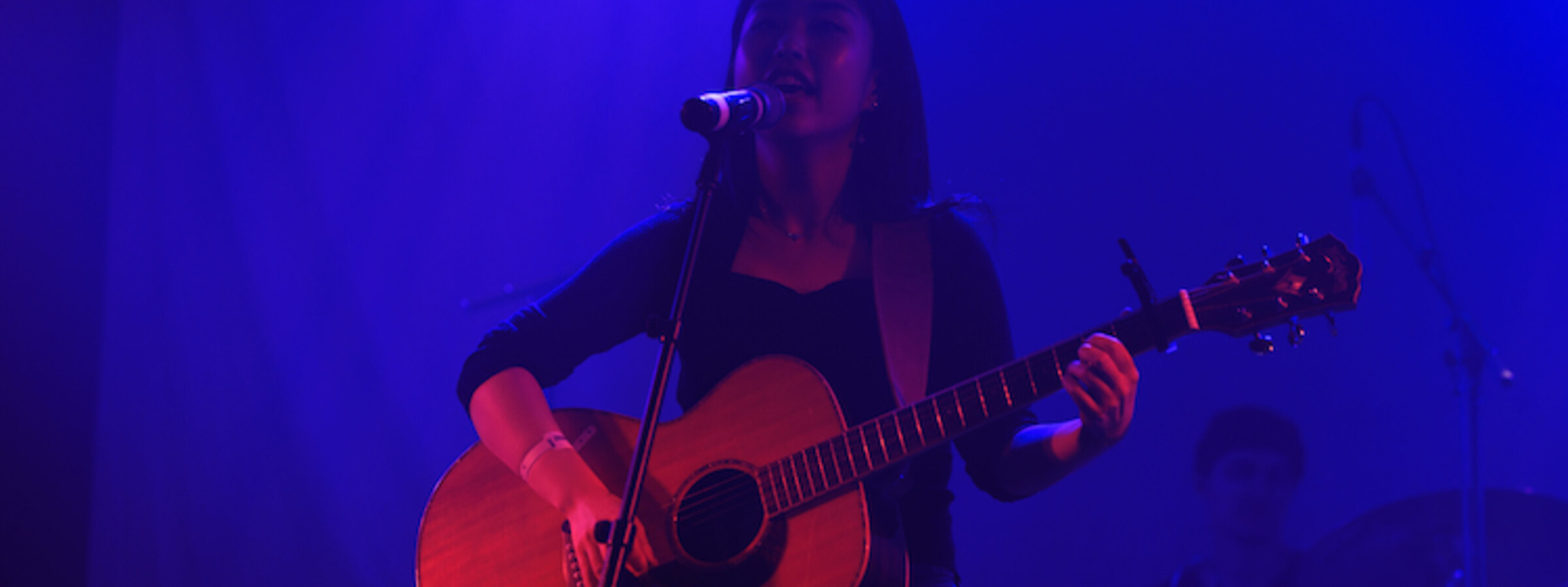 A woman plays an acoustic guitar on a blue-lit stage in a nightclub