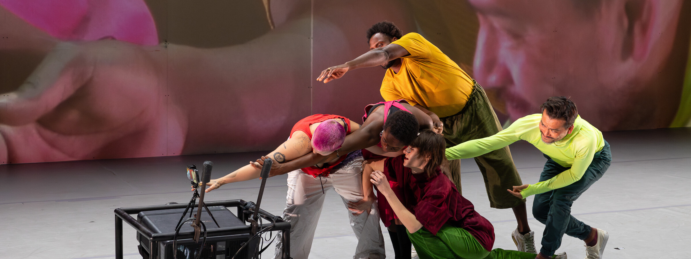 Group of people on stage posing in front of a camera as their image is projected on the wall behind them