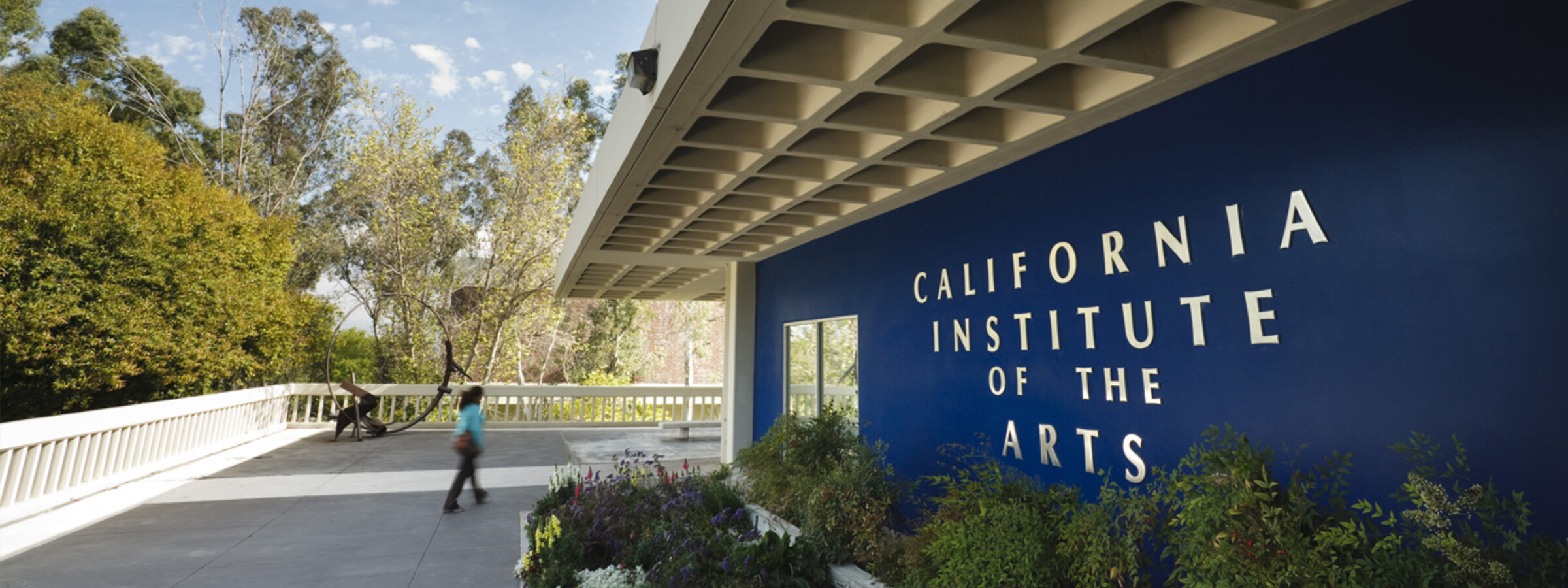 A student walks in front of the Blue Wall at CalArts. the sun is shining in the courtyard.