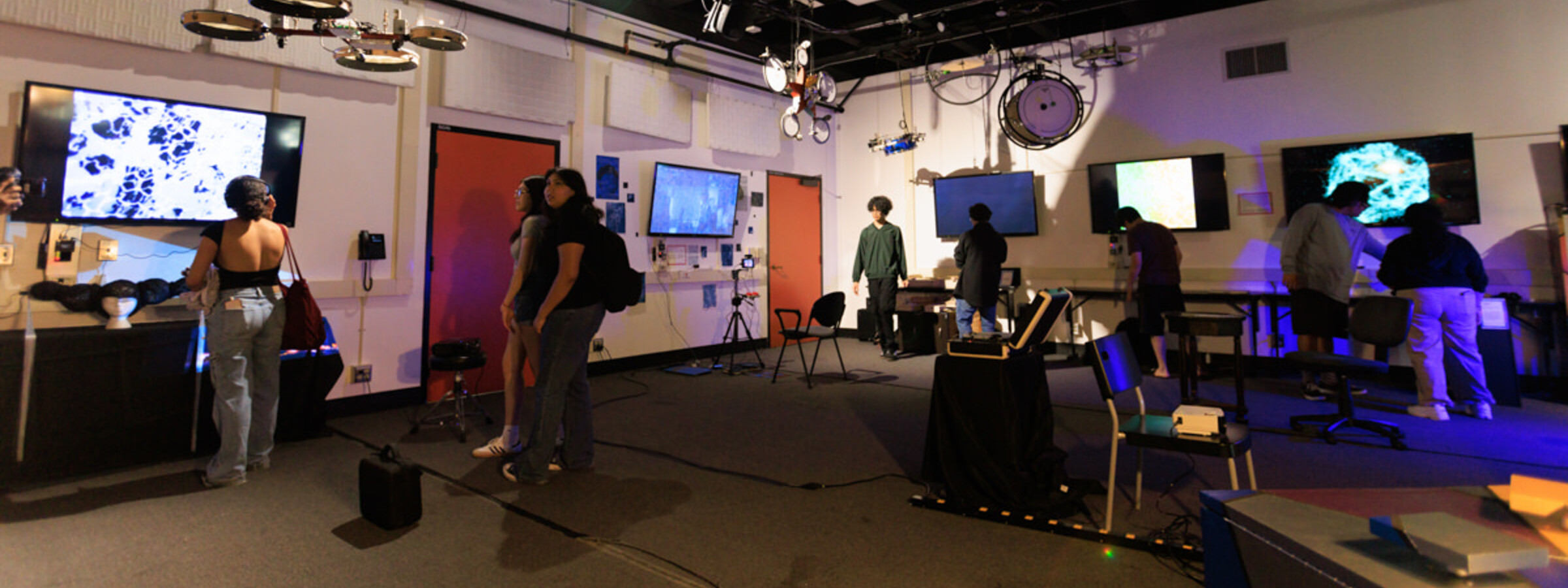 Indoor laboratory with people interacting with various monitors and technical equipment.