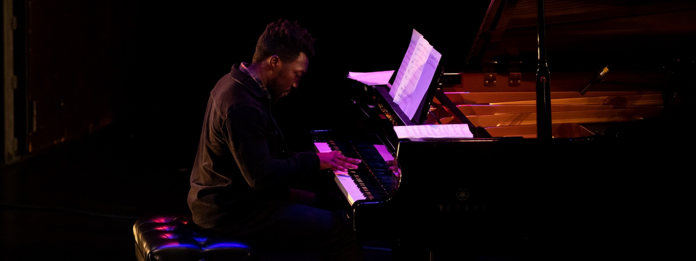 A close-up side view of a man playing a grand piano on a stage 